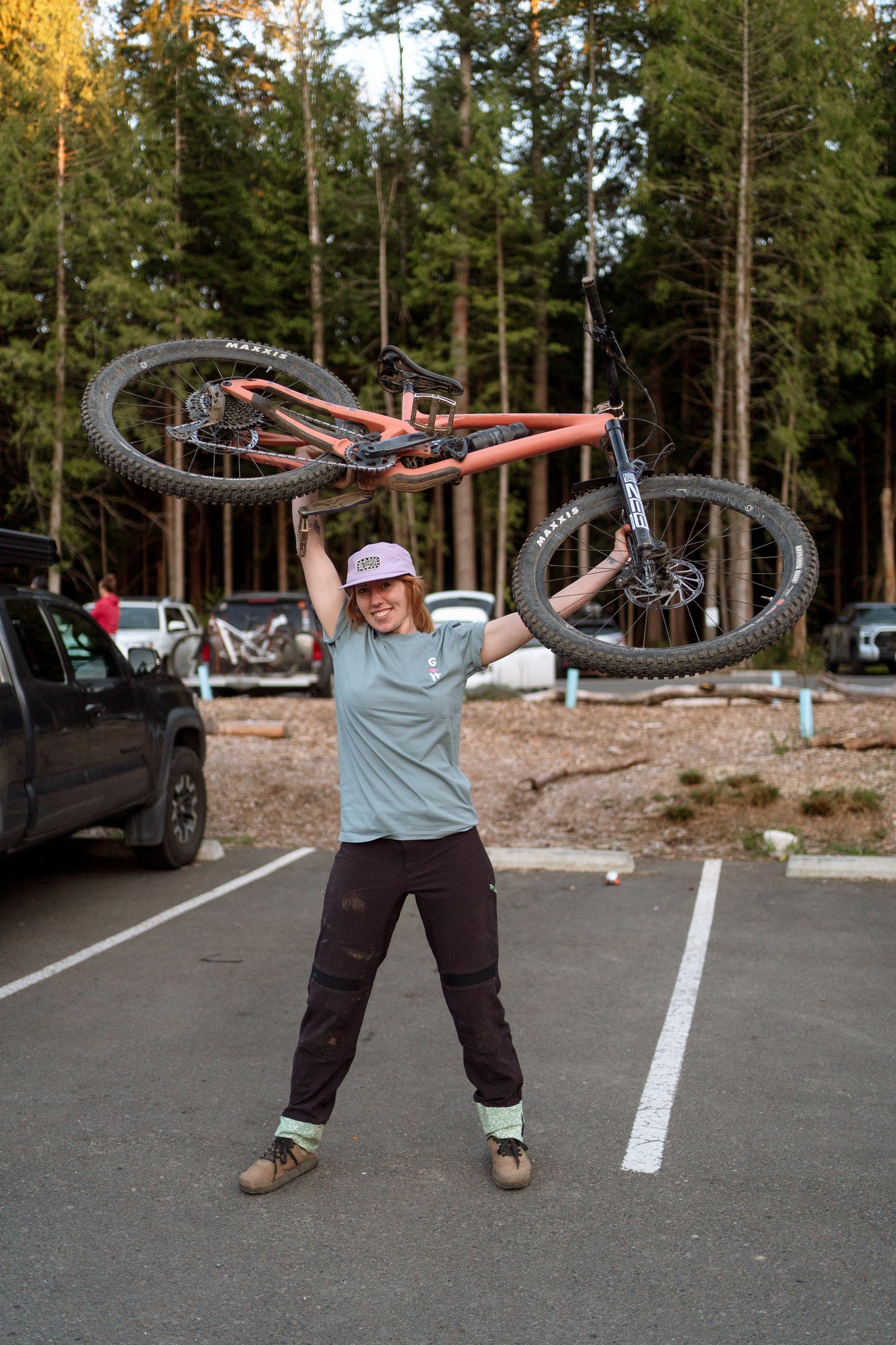 Person holding a bicycle above their head in a parking lot with trees in the background