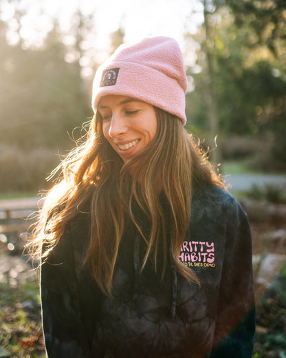 Woman wearing a pink beanie and black jacket with visible text outdoors