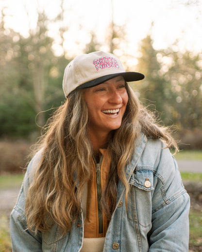 Woman wearing a 5-panel hat with a  gritty habits logo in a natural setting