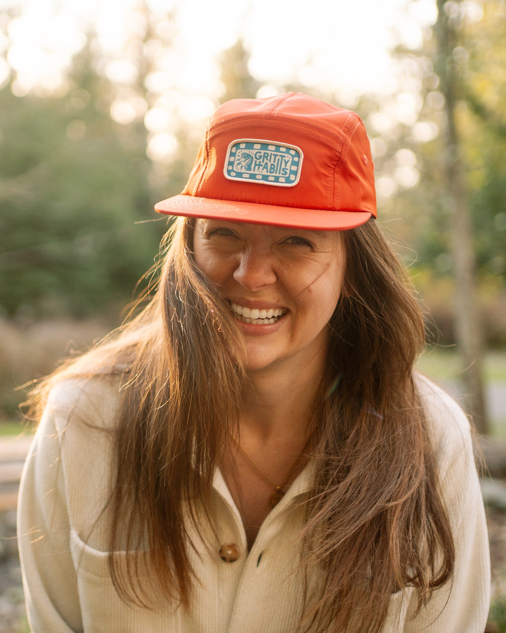 Person wearing an orange cap with a logo, standing outdoors with trees in the background