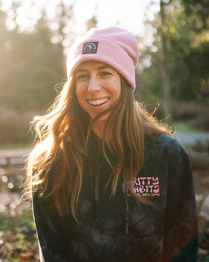 Person wearing a pink beanie and black jacket with visible branding outdoors