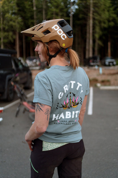 Person wearing a helmet and 'Gritty Habit' t-shirt in a parking lot with trees in the background