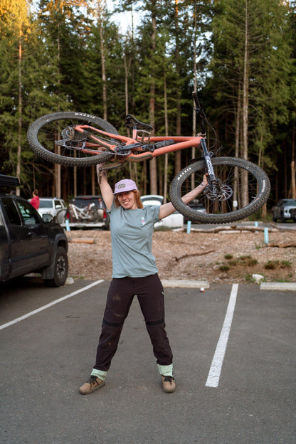 Person holding a bicycle above their head in a parking lot with trees in the background